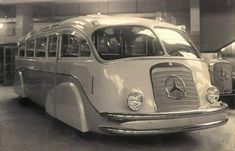 an old bus is parked in a garage with other cars behind it and people standing around