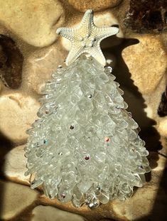 a small glass christmas tree sitting on top of a pile of rocks next to a starfish