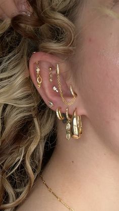 a close up of a person with ear piercings on their ears and wearing gold jewelry