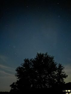 the night sky is lit up with stars and trees in front of a dark building