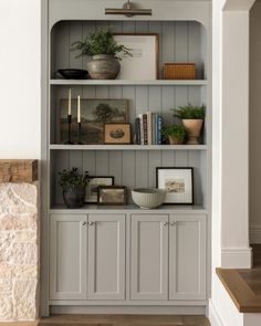 an open bookcase with books and plants on it in the corner of a room