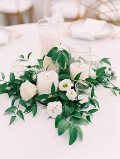 white flowers and candles are arranged on a table with greenery in the foreground