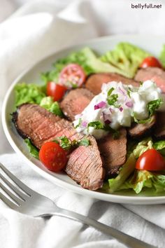 a white plate topped with steak and lettuce next to a knife and fork