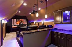 a home theater with purple lighting and black leather couches in front of the screen