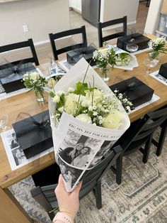 a person is holding flowers in front of a table with black and white place settings