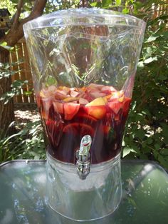 a glass container filled with fruit sitting on top of a green table next to trees