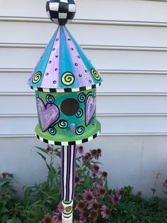 a colorful birdhouse sitting on top of a flower bed in front of a house