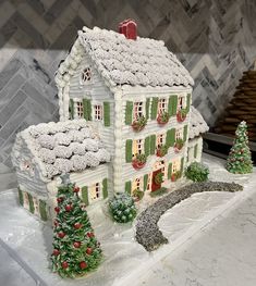 a white christmas house with green shutters and snow on the roof next to trees