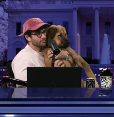 a man sitting at a desk with a dog on his lap and a microphone in front of him