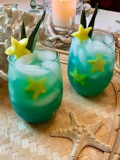 two glasses filled with blue liquid sitting on top of a table next to a starfish candle