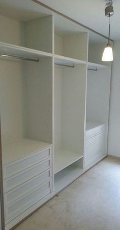 an empty walk in closet with white cabinets and drawers on the bottom shelf, next to a lamp