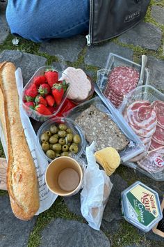 the food is laid out on the ground with bread, strawberries, olives and meat