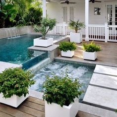 an outdoor hot tub surrounded by potted plants next to a deck with water running down it