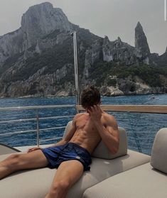 a shirtless man sitting on top of a boat in the ocean next to mountains