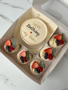 a birthday cake in a box with cupcakes and strawberries