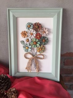 a frame with some flowers in it and pine cones on the table next to it