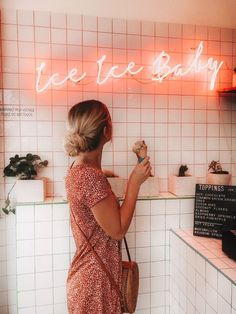 a woman standing in front of a pink neon sign that says ice cream baby on it