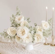 white flowers are in a vase on a table with candles and other decorations around it