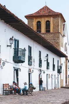 several people sitting on benches in front of a white building with an old clock tower