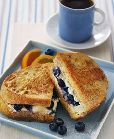 a blueberry sandwich cut in half on a plate next to a cup of coffee