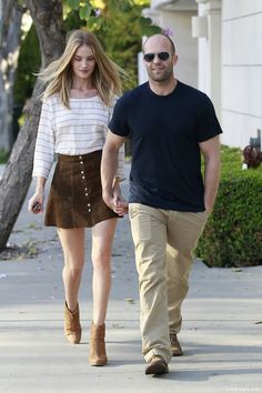 a man and woman walking down the street holding hands with one another, both wearing brown suede skirts