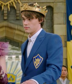 a young man in a blue suit and crown standing next to a woman wearing a purple dress