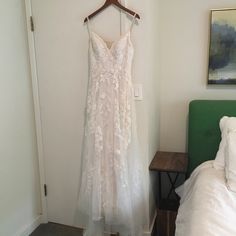 a wedding dress hanging on a hanger in a room with a bed and green headboard