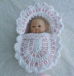 a baby doll is in a crocheted white and pink outfit on a blanket