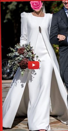 a woman in a white dress with a pink flower on her head and a man in a suit walking behind her