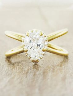 a yellow gold ring with a pear shaped diamond in the center on a wooden surface