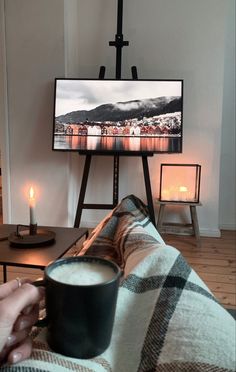 a person holding a coffee cup in front of a flat screen tv on a stand