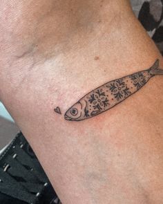 a small fish tattoo on the wrist is shown in black and grey ink, with flowers around it