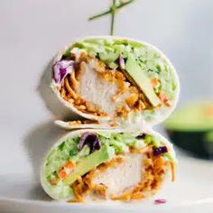 two burritos on a white plate with avocado and shredded carrots