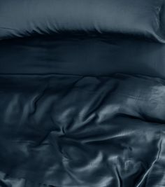 an unmade bed with dark blue sheets and pillowcases on top of it