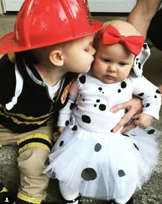 two children dressed up as firemen kissing each other's cheek while sitting on the ground