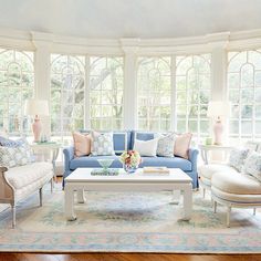 a living room filled with lots of furniture next to two large windows and a rug on the floor