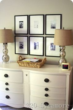 a white dresser topped with lots of drawers next to two lamps and pictures on the wall