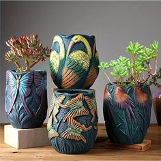 three vases with plants in them sitting on a wooden table next to each other