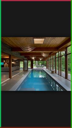 an indoor swimming pool in the middle of a room with large windows and wood ceilinging