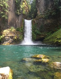 there is a waterfall in the middle of this river with green moss growing on it