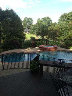 an outdoor swimming pool surrounded by wooden decking and fenced in area with table and chairs