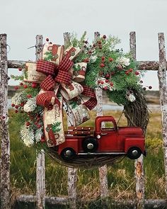 a red truck with a wreath on it is sitting in front of a wooden fence