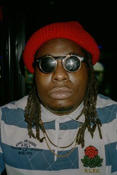 a man wearing sunglasses and a red hat with dreadlocks is looking at the camera