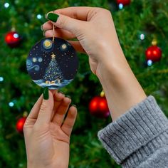 a person holding up a christmas ornament in front of a christmas tree with lights