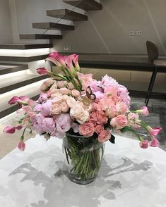 a vase filled with pink and white flowers on top of a table next to stairs