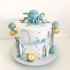 a white cake with blue and gold decorations on the top is decorated with an octopus