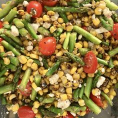 a salad with asparagus, tomatoes, corn and feta cheese on it