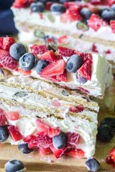 two slices of cake with strawberries and blueberries on top, sitting on a cutting board