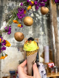 a hand holding an ice cream cone with flowers hanging from the ceiling in front of it