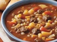 a blue bowl filled with pasta and meat soup on top of a wooden table next to bread